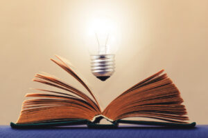 Light bulb glows brightly over an open book symbolizes the emergence of the idea