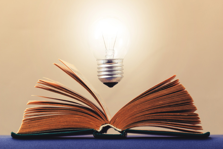 Light bulb glows brightly over an open book symbolizes the emergence of the idea